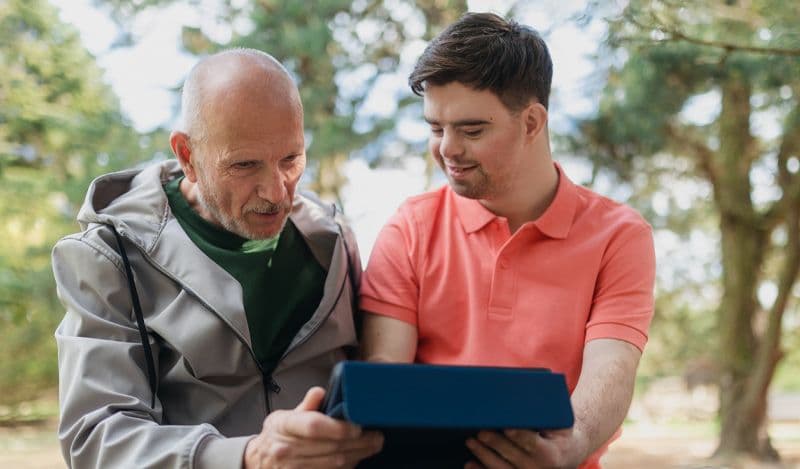 Father and song use electronic tablet while outside in a park