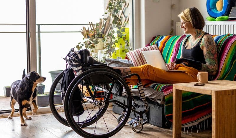 Woman in specialized wheelchair in apartment with a small dog looking at her