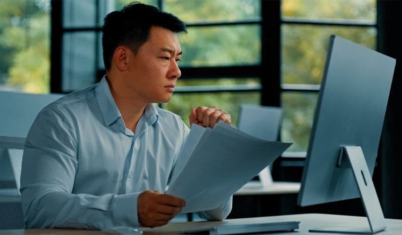 Asian man working at desk with hand full of papers
