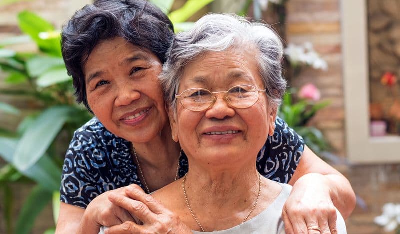 Two elderly women smiling looking toward the camera while outside